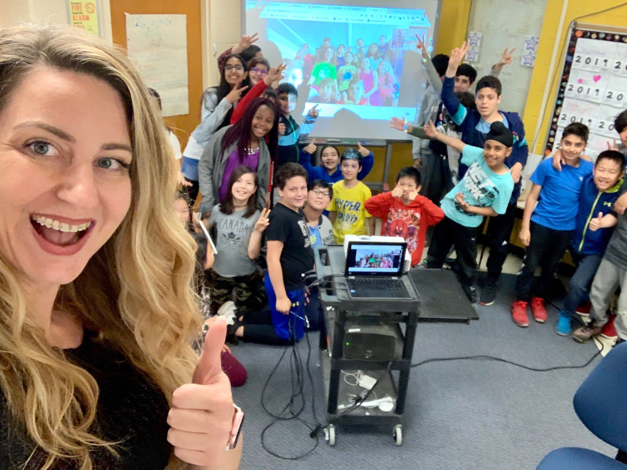 A teacher and her students are waving with their partner class from a live virtual exchange.