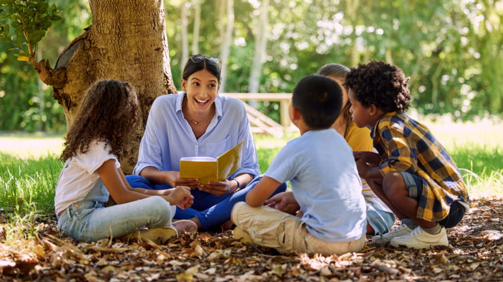 The image shows a group of students listening to a story outdoors.